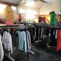 Winkelinterieur met meerdere kledingrekken vol tweedehands kleding, goed verlichte ruimte met hoge plafonds