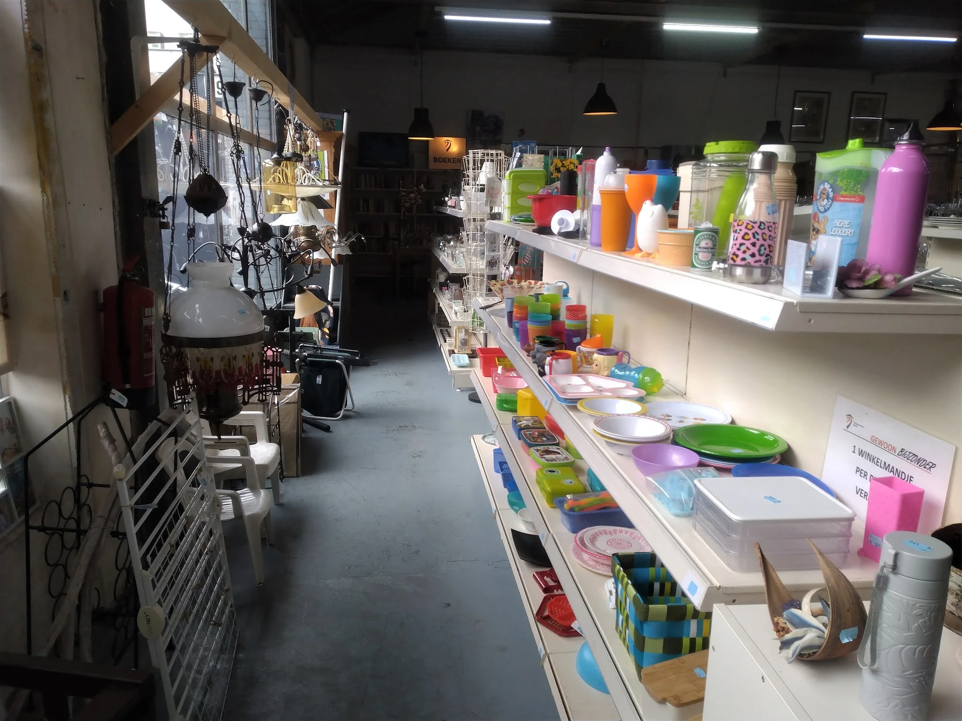 Winkelvloer van kringloopwinkel met stellingen vol huishoudelijke artikelen, keukengerei en decoratieve items in verschillend