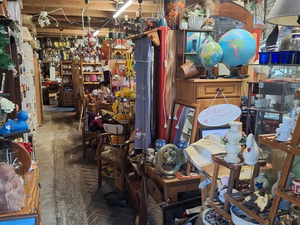 Brocantewinkelbinnenkant met houten meubels, globes, lampen en diverse vintage spullen op stellingen