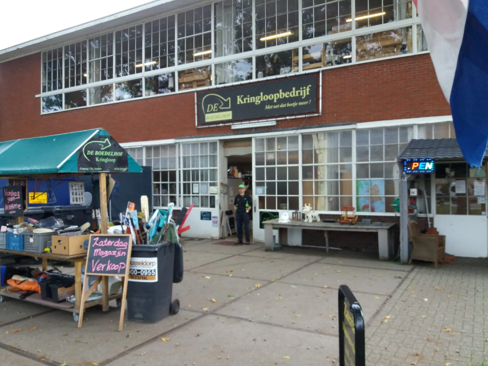 Gevel van kringloopwinkel met etalage, ingang en terras met uitgestalde spullen