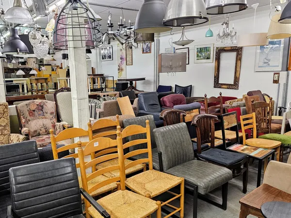 Winkelvloer met diverse meubels: houten stoelen met rietvlechting, fauteuils, tafels en hangende lampen