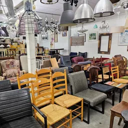 Winkelvloer met diverse meubels: houten stoelen met rietvlechting, fauteuils, tafels en hangende lampen