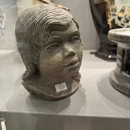 Stenen beeldhouwwerk van een vrouwenhoofd met golvendes haar, close-up op displaytafel
