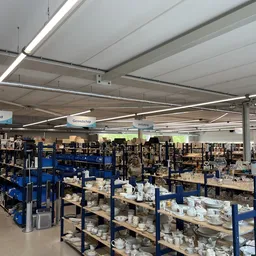Ruim magazijn met blauwe stellingkasten vol huishoudartikelen en serviesgoed, moderne plafondverlichting