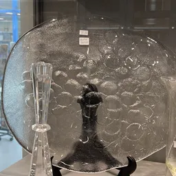 Glazen schaal met reliëfpatroon en zwarte voet, tentoongesteld op een standaard