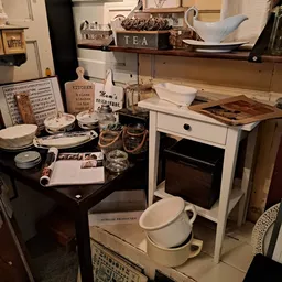 Kringloopwinkel interieur met huishoudartikelen: zwarte tafel met servies, witte fornuis, planken met decoratieve items en ke