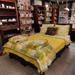 Tweepersoonsbed met geel-wit beddengoed en decoratieve kussens in een ingerichte slaapkamer