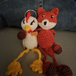 Twee gehaakt speelgoed dieren: een wit/geel kippen-keychain en een rood vosje, dicht tegen elkaar aan