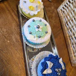 Drie decoratieve cupcakes met gekleurde frosting en metallic bolletjes in een doosje
