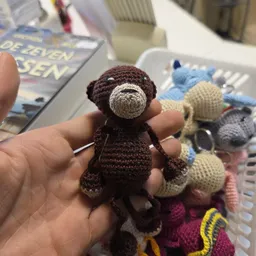 Kleine gehaakt bruine teddybeer in hand, op achtergrond meer gekleurde gehaakt speelgoed