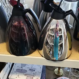 Twee zwarte koffiezetapparaten met reflecterende oppervlakken op een plank