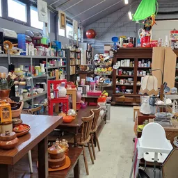Overzicht van de winkelvloer met houten meubels, serviesgoed, boeken en diverse huishoudelijke artikelen op stellingen en taf
