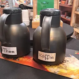 Twee thermoskannen met labels 'Thee' en 'Koffie' op een oranje ondergrond in een kringloopwinkel