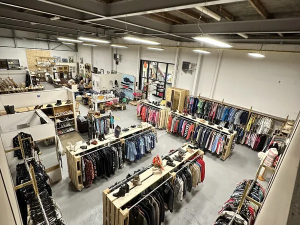 Overzicht van kringloopwinkel met rekken vol tweedehands kleding, tafels met uitgestalde spullen en diverse afdeling