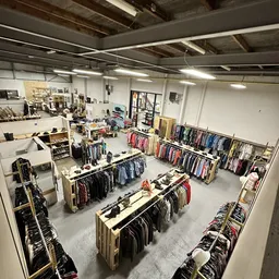Overzicht van kringloopwinkel met rekken vol tweedehands kleding, tafels met uitgestalde spullen en diverse afdeling