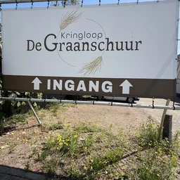 Gevel van kringloopwinkel De Graanschuur met ingangsaanduiding en graarnaam op bord