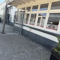 Voorgevel van kringloopwinkel met grote ramen, metalen toegangshek en straatwerk