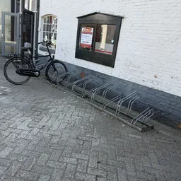 Voorkant van kringloopwinkel met witte gevel, zwarte deur en fietsenstalling met enkele fiets
