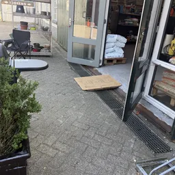 Ingang van kringloopwinkel met houten oprit, stapels witte handdoeken en spullen buiten