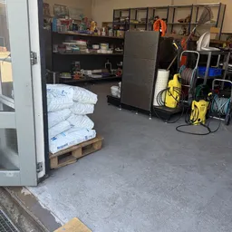Binnenkant van kringloopwinkel met witte matrassen op pallet, gele reinigingsapparatuur en diverse stellingen