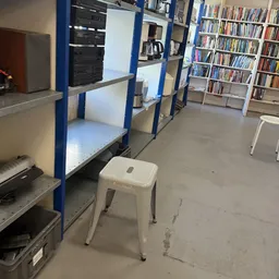 Winkelinterieur met blauwe stellingen, boekenkasten en een witte kruk op de vloer