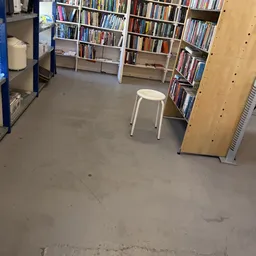 Winkelvloer met boekenkasten en een witte kruk in een kringloopwinkel