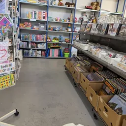 Winkelvloer met blauwe stellingen vol boeken en spullen, kartonnen dozen op de grond, witte wandrekken met merchandise aan de