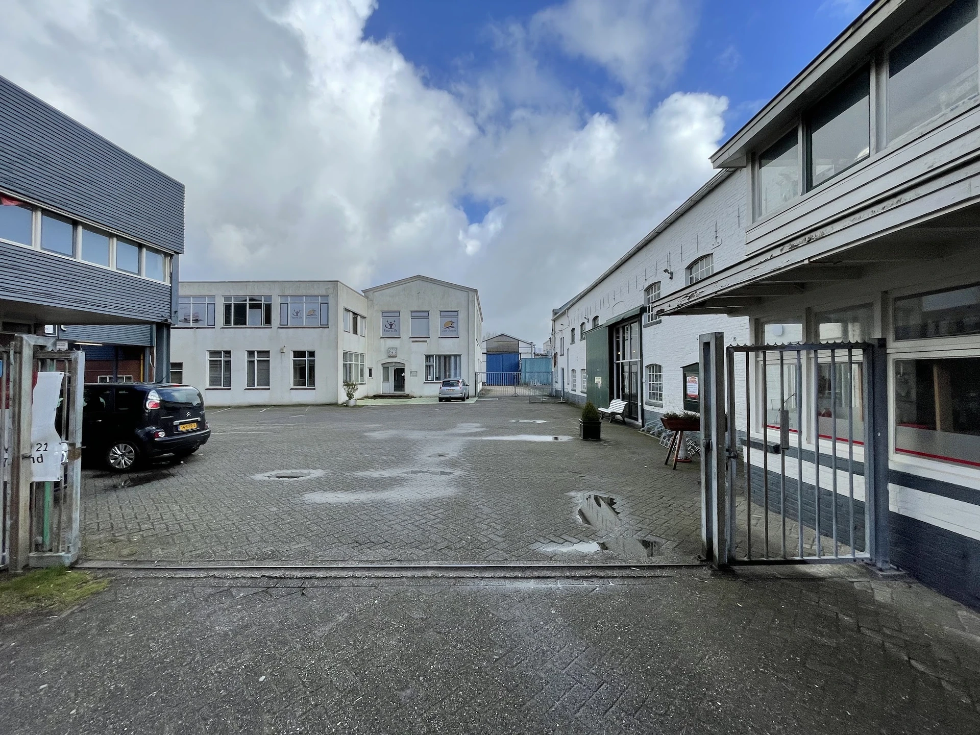 Binnenplaats met grijze tegels omgeven door diverse industriële gebouwen onder bewolkte hemel