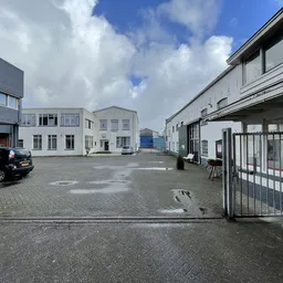 Binnenplaats met grijze tegels omgeven door diverse industriële gebouwen onder bewolkte hemel
