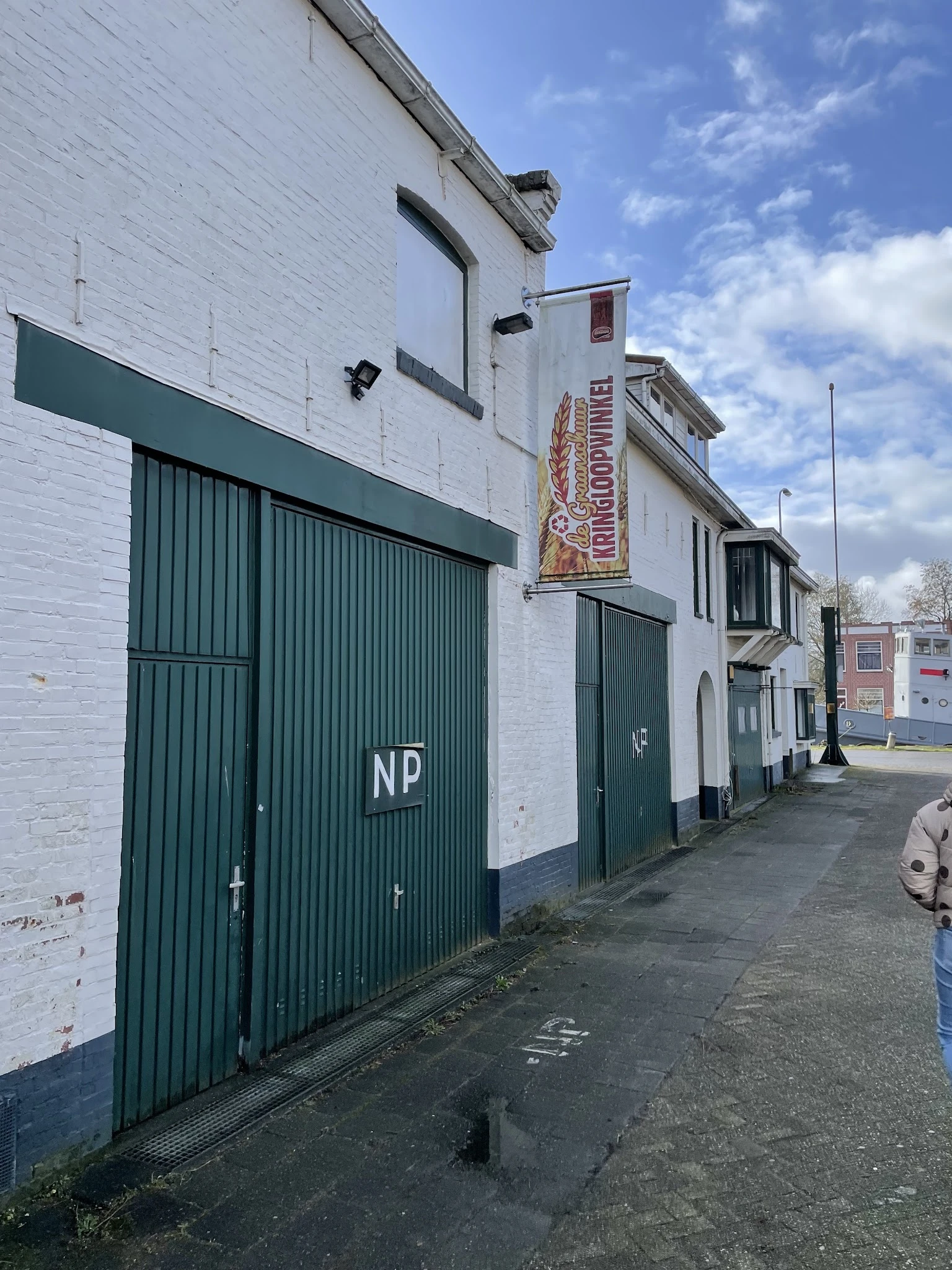 Witte bakstenen gevel van kringloopwinkel met groene metalen deuren en 'NP' markering, aan een straat