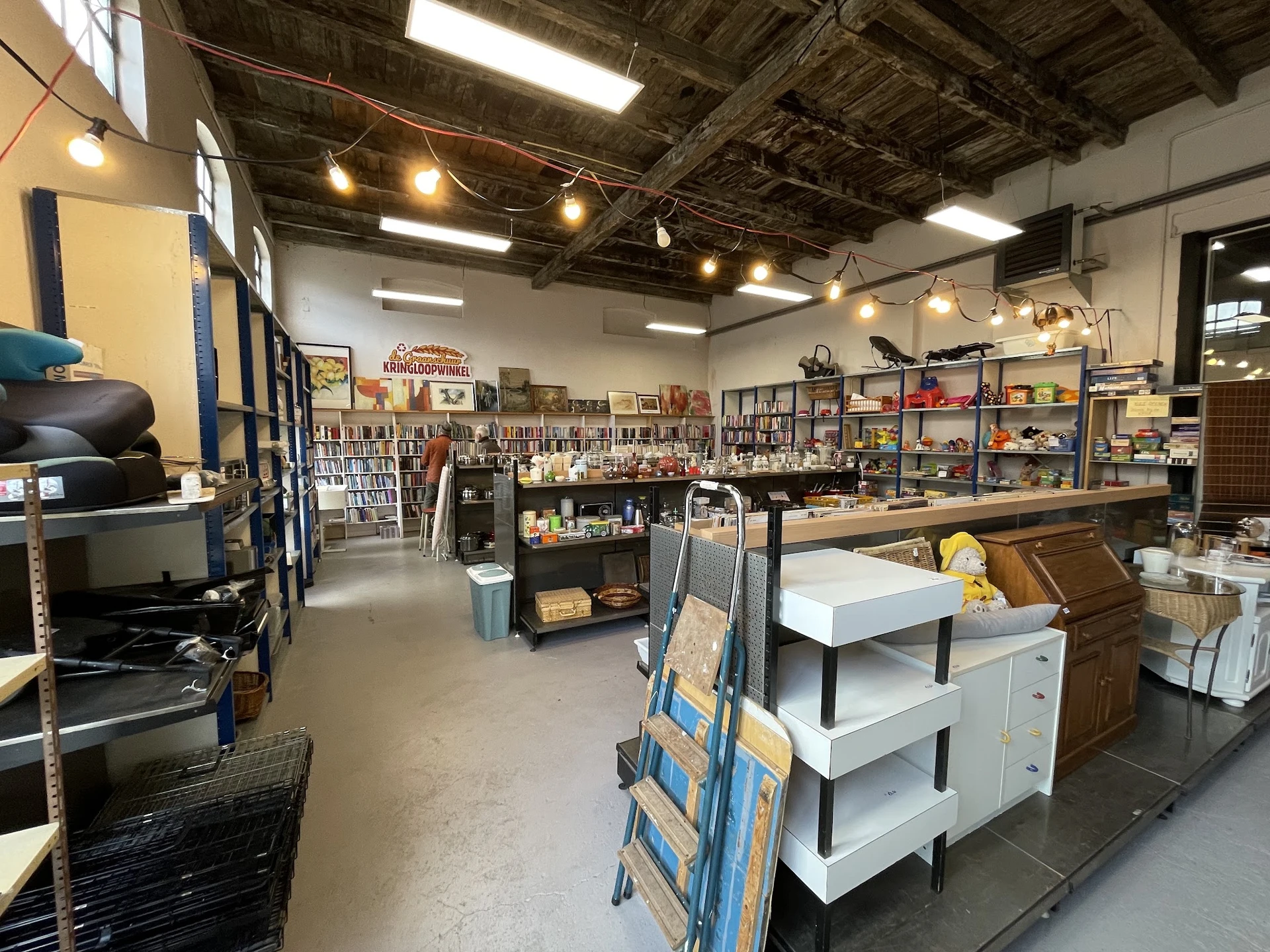 Winkelvloer met stellingen vol spullen, toonbanken en diverse tweedehands artikelen in een ruime kringloopwinkel