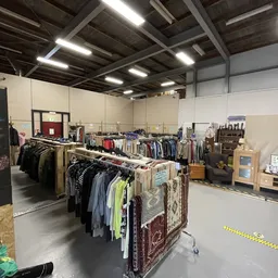 Ruime winkelruimte met kledingrekken en tweedehands artikelen, industriële plafondverlichting