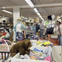 Winkelvloer met kledingrekken, etalagepoppen en diverse kleding- en huishoudartikelen, bezoekers lopen door de winkel