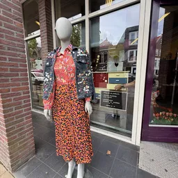 Etalagepop met tweedehands dameskleding: rode blouse met bloemenprint en oranje jurk met zwart patroon