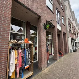 Gevel van kringloopwinkel met etalage vol kleding en accessoires aan het raam