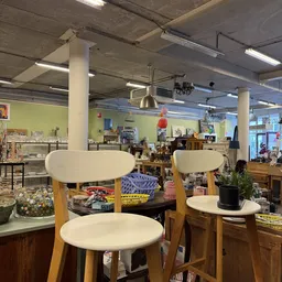 Winkelvloer met houten stoelen met witte zitting, stellingen vol spullen en gele muren