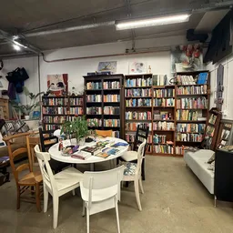 Binnenkant kringloopwinkel met grote boekenkasten, witte ronde tafel met stoelen en verschillende spullen op de vloer