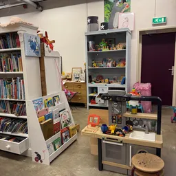 Speelhoek in kringloopwinkel met boeken, speelgoed, keukentje en verschillende stellingen met verzamelde spullen