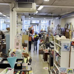 Winkelvloer van kringloopwinkel met stellingen, huisraad en bezoekers aan het winkelen
