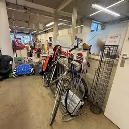 Fietsen en fietsaccessoires in een kringloopwinkel, met trapjes en ander materieel op de achtergrond