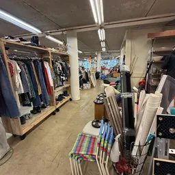 Winkelvloer met kledingrekken, stellingen met diverse spullen en een centrale kolom in een kringloopwinkel