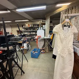 Werkruimte in kringloopwinkel met computer, stellingen, kleding op hangers en diverse spullen