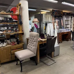 Winkelvloer met houten kasten, kledingrekken, een grijze stoel en diverse tweedehands spullen en meubels
