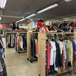 Winkelvloer met houten rekken vol tweedehands kleding, toonbank met jurken en accessoires achter