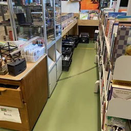 Winkelgangetje met stellingen vol boeken en media aan beide zijden, groene vloer, zwarte kratten in het midden