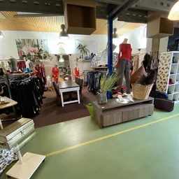 Winkelvloer van kringloopwinkel met kledingrekken, etalagepop in rood shirt, toonbank en stellingen met diverse spullen