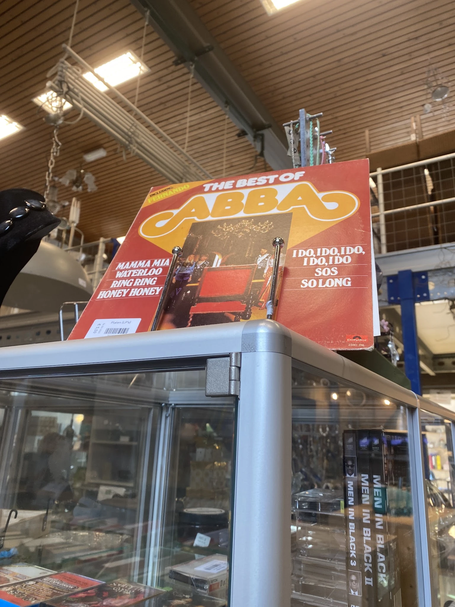 ABBA 'The Best Of' vinyl LP in rood en geel kartonnen hoes, bovenkant van display case zichtbaar