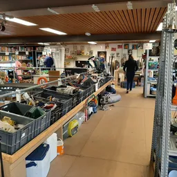 Overzicht van de winkelvloer met stellingen, zwarte kratten met spullen, kasten met artikelen en bezoekers in de kringloopwin
