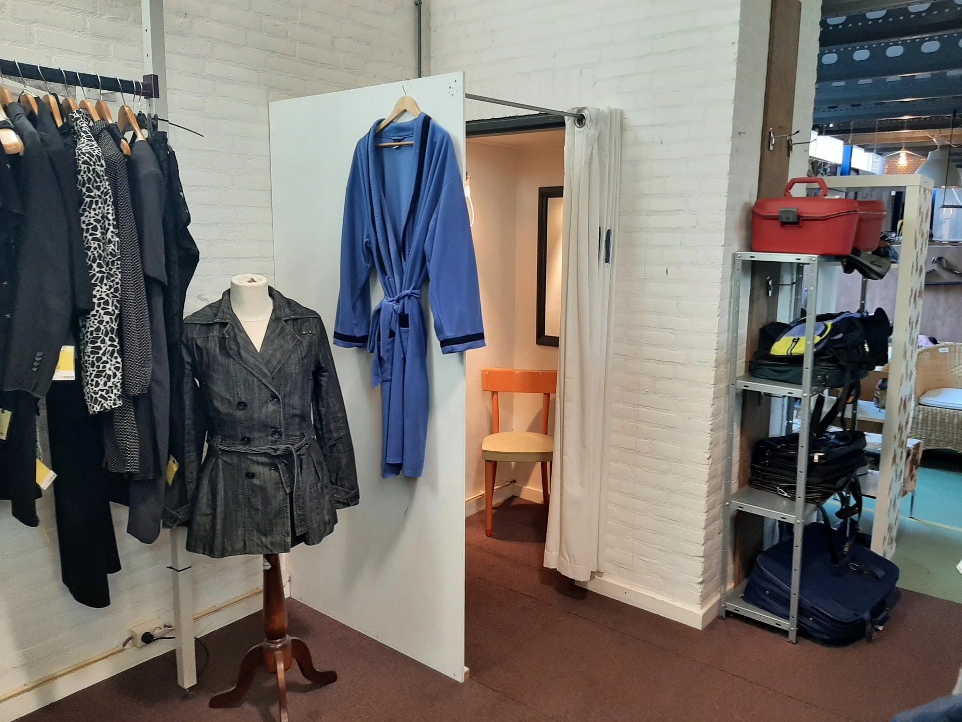 Winkelinterieur met kledingrekken, pashokje en stellingen met tweedehands spullen