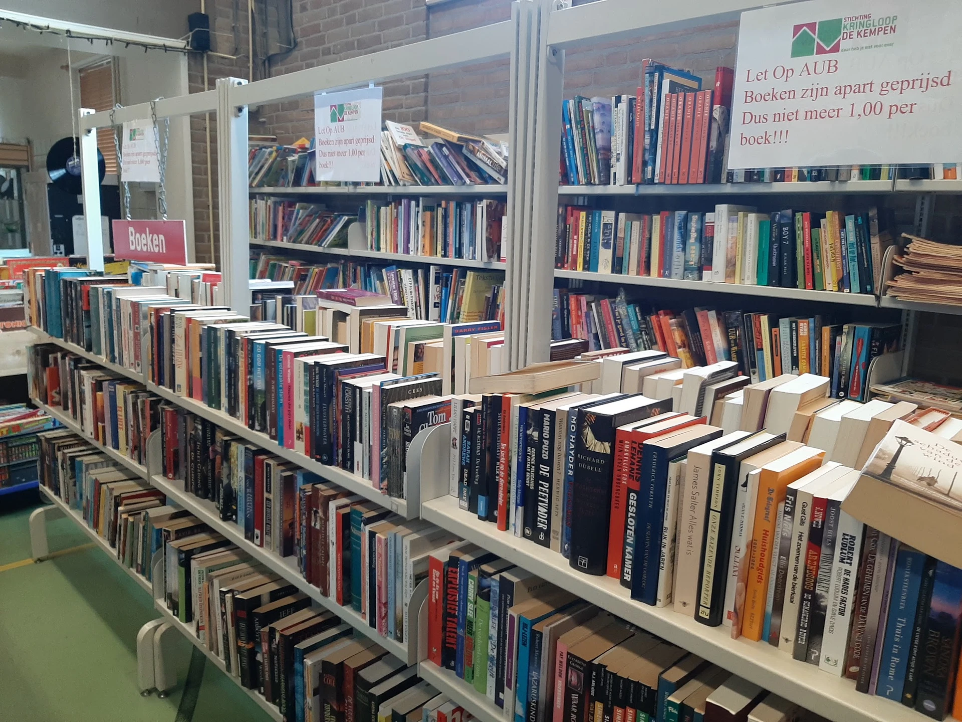 Stellingen vol met tweedehands boeken, gerangschikt op een lange tafel in de winkel